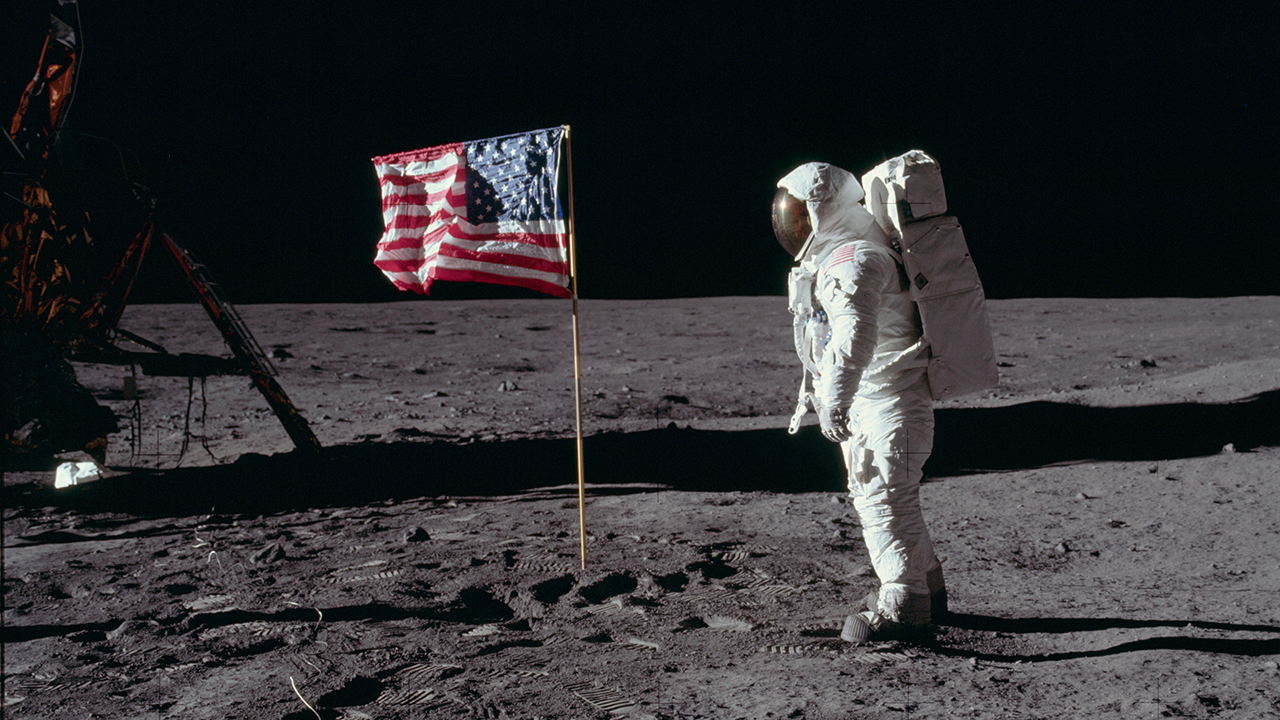 Ein Astronaut der Apollo 11 Mission steht neben der soeben gehissten US-Amerikanischen Flagge.